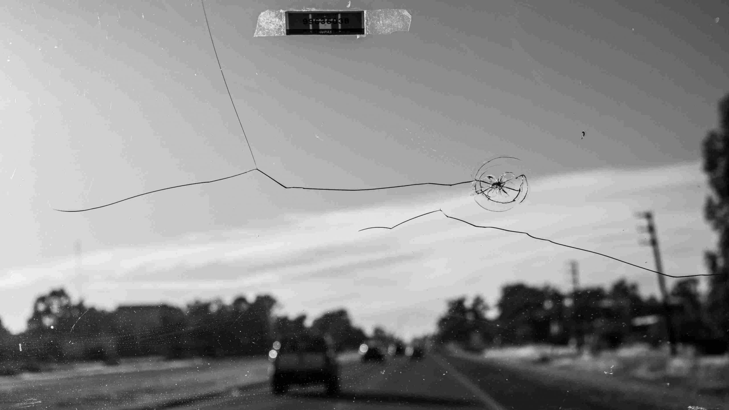 A cracked windshield of a vehicle driving along a roadway.