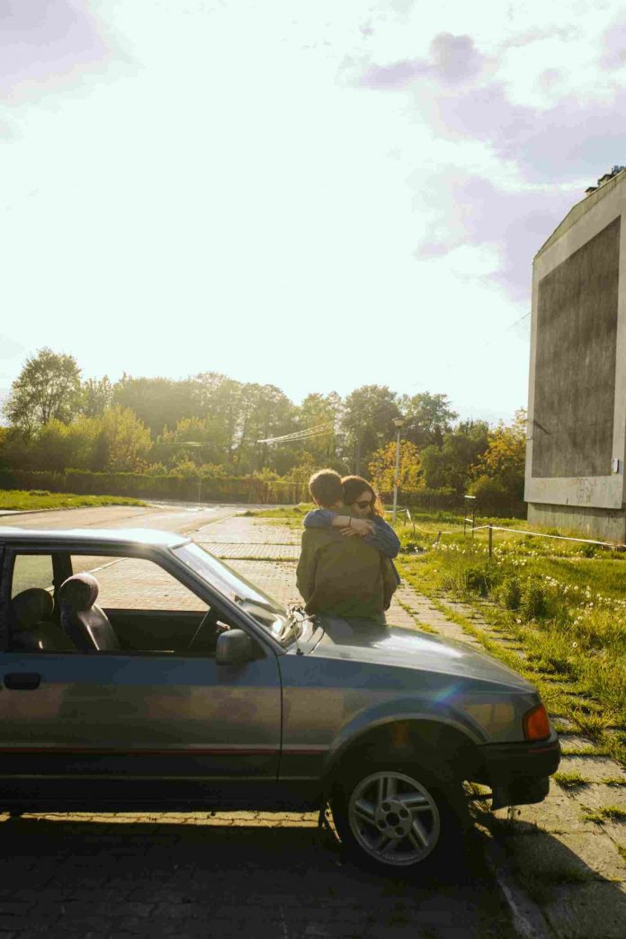 A man and a woman hugging on the hood of a parked car.